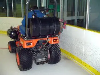 A large orange and black tractor parked on the side of an ice rink.