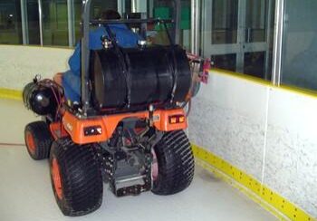 A large orange and black tractor parked on the side of an ice rink.